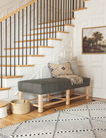 #color::loden | The ambleside loden gray linen bench sits by a staircase against white accented walls near a black and white patterned rug