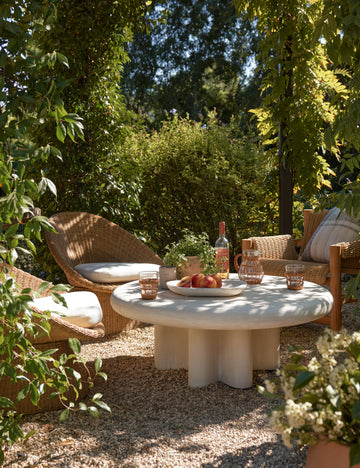 #color::ivory | Ruiz round cement outdoor coffee table styled with wicker accent chairs in an outdoor lounge space.