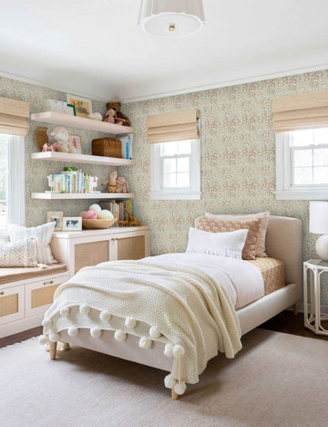 #color::warm | Warm-toned Floral Field Wallpaper by Rylee + Cru is in a child's bedroom with a toy-filled shelf and a bed with a pom pom throw blanket