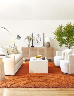 The Arches rust orange rug lays in a living room under an ivory sofa and two ivory swivel chairs