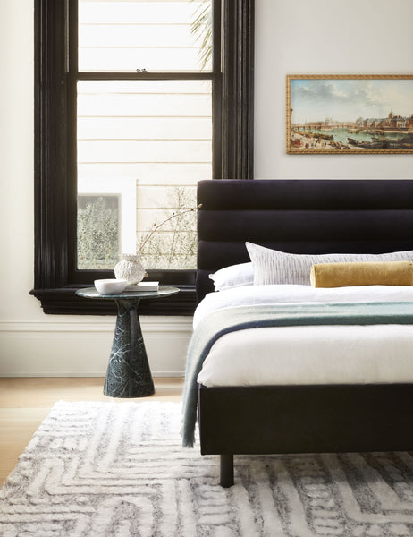 #color::navy-velvet #size::twin #size::full #size::queen #size::king #size::cal-king | The Bailee Navy Velvet platform bed lays in a bedroom next to a black framed window atop a patterned rug