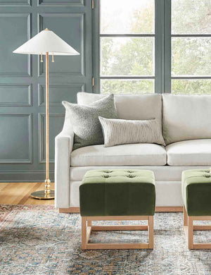 The Manon linen moss green square boucle pillow sits on a white sofa in a living room with green accented walls and green velvet ottomans