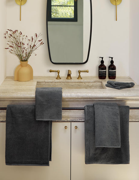 #color::shadow | The Midnight gray dune turkish cotton Air Weight Towel Set by Coyuchi hangs off of a concrete sink in a bathroom with a narrow black framed mirror and a sculptural yellow vase