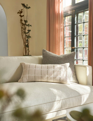 The Manon linen slate gray square boucle pillow sits on a cream linen sofa behind a lumbar throw pillow in a living room with blush pink curtains