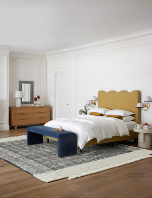 The Joelle black rug lays in a colorful bedroom under a golden linen sculptural bed and a navy linen bench