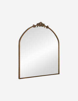 Angled view of the Tulca arched gold mirror with flat bottom edge and traditional scroll detailing.