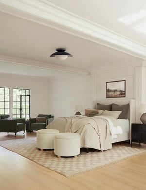 The Irregular beige checkerboard rug by Sarah Sherman Samuel sits in a bedroom with a talc linen adara bed and two upholstered ottomans all sitting atop a light wood hardwood floor.