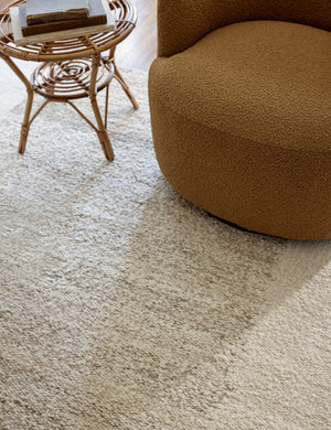 Close up of the Woburn rug under an ochre boucle swivel chair and woven side table