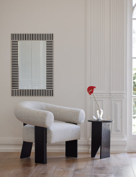 #color::black | The Celeste black wood accent chair with wishbone frame sits in a bright room with a black wood side table, a black and white stripe framed mirror, and a sculptural candle holder.