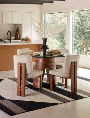 Four Sydney Dining Chairs sit around a circular dining table atop a black, gray, and cream geometric rug with a black vase centerpiece