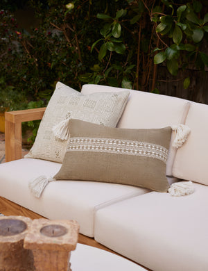 Marchesa moss green indoor and outdoor lumbar pillow with tasseled corners sits on a natural linen sofa in an outdoor space