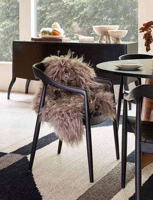 The Vale icelandic light gray sheepskin sits in dining room atop a black dining chair