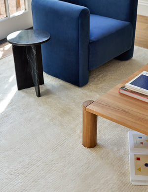 The Noa Moroccan Shag Rug sits under a blue velvet accent chair, a square wooden coffee table, and a black marble side table