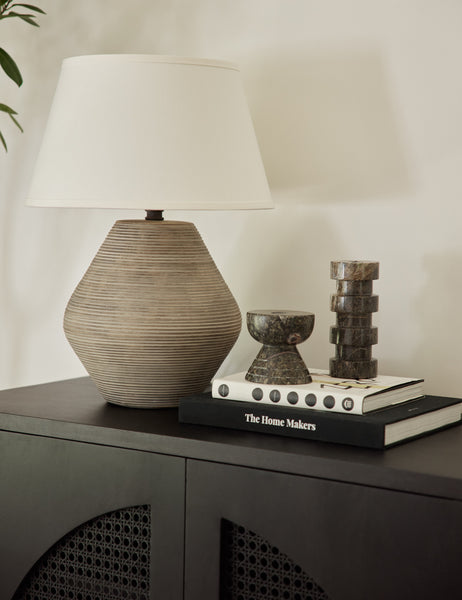 | A Khala table lamp with ribbed base and weathered finish sits atop a black side table with black marble sculptural decor and a stack of two books