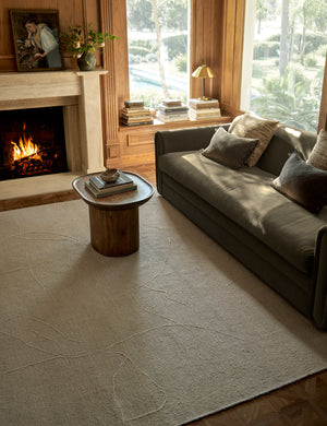 The beachwood rug lays in a dark living room with wooden walls under a wooden side table and a green velvet sofa