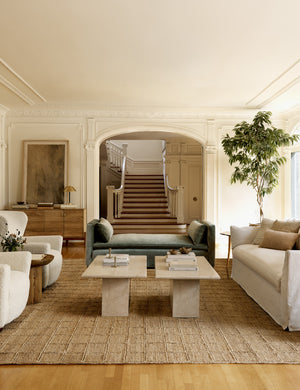 The Harper rug lays in a living room with accented walls under two stone coffee tables and ivory furniture