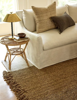 The wilcox rug sits underneath a natural linen slipcover sofa and a rattan cane side table with a brass lamp