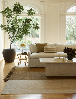 The wilcox rug sits underneath a natural linen slipcover sofa and a rattan cane side table with a brass lamp