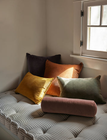 #color::moss #style::lumbar #fill type::with-feather-down-insert #fill type::pillow-cover-only | Charlotte velvet pillow in mustard, burnt orange, warm gray, and moss sit together on a striped cushioned bench