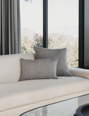 The manon linen slate gray boucle pillow in both sizes lay on a white linen sofa in a living room with an oval coffee table