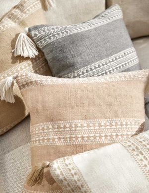 Marchesa sandstone indoor and outdoor pillow with tasseled corners lays amongst other Marchesa throw pillows