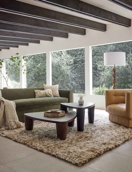 #size::6--x-9- #size::8--x-10- #size::9--x-12- #size::10--x-14- #size::12--x-15- | The tegan moroccan shag rug lays in a living room with wooden beamed ceilings under a green velvet sofa and nested coffee tables