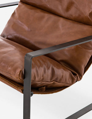 Close-up of the right metal arm of the brown leather Marlyne sling-back accent chair with black metal frame