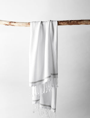 The Mediterranean Turkish Cotton white Guest Towel by Coyuchi with tasseled ends hangs off a branch
