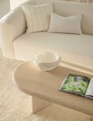 Charlotte oyster white lumbar velvet pillow sits on a cream sofa behind a light wooden oval coffee table