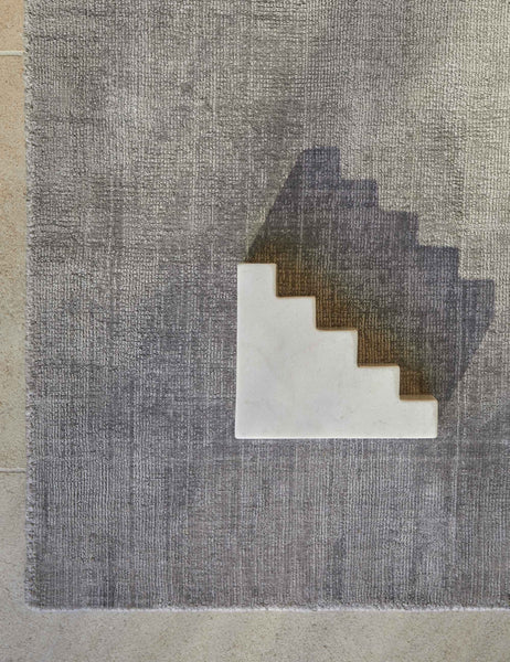 #color::gray #size::6--x-9- #size::8--x-10- #size::9--x-12- #size::10--x-14- #size::12--x-15- | Bird's-eye view of the corner of the gray dylan rug with a staircase shaped white sculptural object sitting atop it
