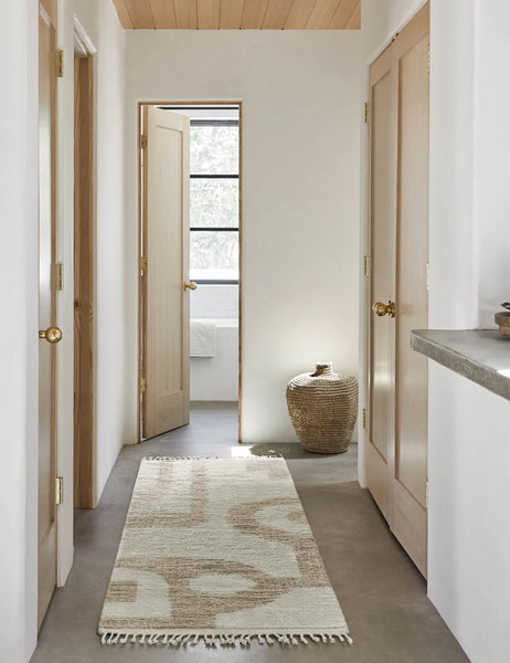 #size::2-6--x-8- | The Nomad neutral-toned geometric floor rug by Élan Byrd with subtle ribbed design in its runner size lays in a hallway with a wooden paneled ceiling, a jute basket, and neutral wooden doors with golden knobs