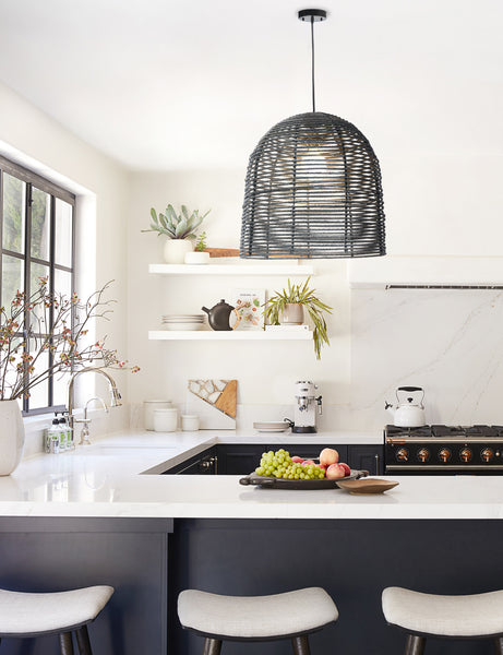 #color::black | The Beehive black jute woven pendant light is hung above a kitchen island with black cabinetry and white countertops