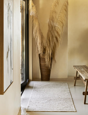 The Taos neutral light brown wool blend runner rug lays in front of a door and across from a low wooden bench.