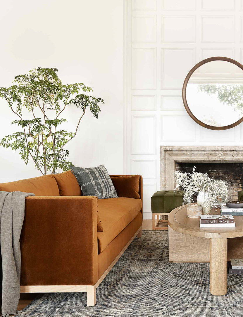#showall::39490223177827| Cognac Velvet Hollingworth Sofa sits in a living room with a dark-toned patterned rug, a green velvet ottoman, and an oval coffee table
