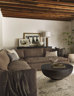 The Portola Mushroom brown linen Slipcover corner sectional Sofa sits atop a plush ivory rug next to a woven chair