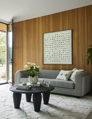 The see through navy and white wall art is hanging on a wood paneled wall in a living room above a gray sofa