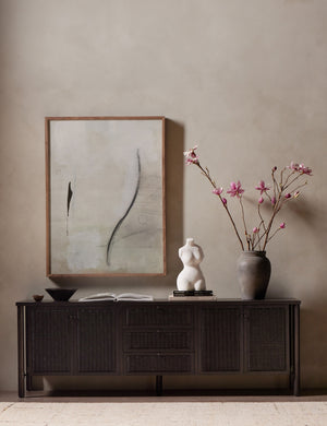 Isaura black cane-paneled media console styled with a large vase, modern wall artwork and sculptural decor.