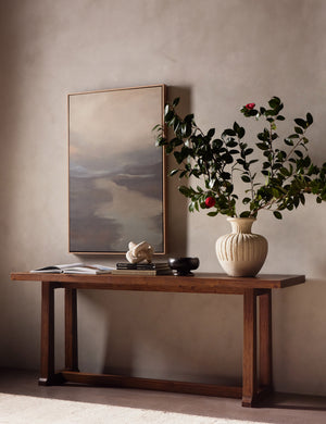 Hayman honey finish solid wood console table styled with a white textural vase filled with botanical stems and a large scale, abstract piece of wall art.