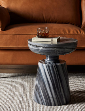Zeller round carved ebony marble side table styled next to a leather sofa atop a grey striped rug.