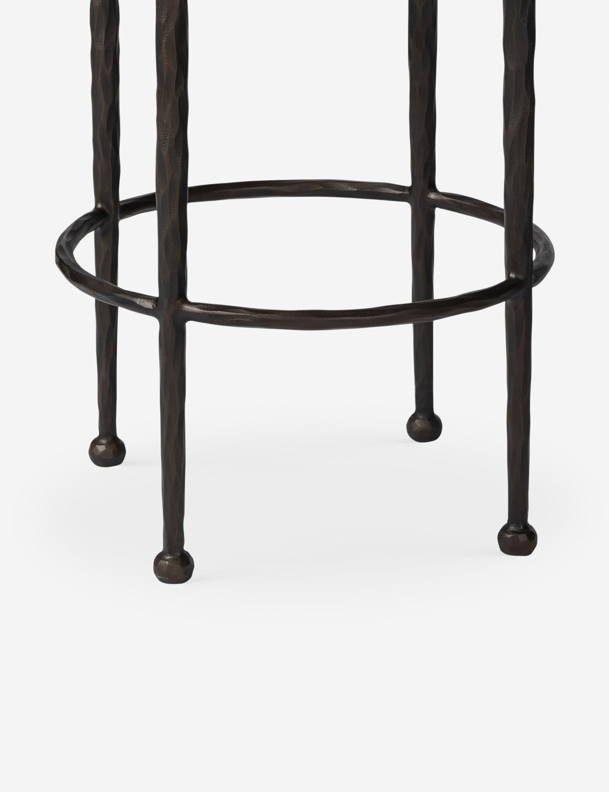 Close-up view of the dark brown hammered metal legs and circular footrest of the stool.
