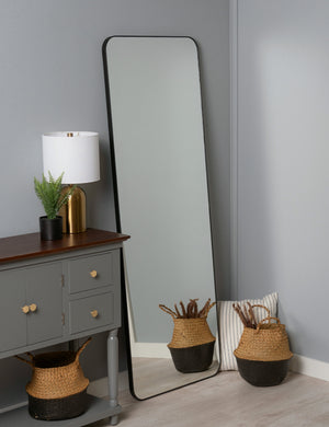 Aire rounded corner leaning floor mirror with black frame leaning against a wall