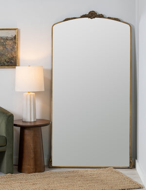 Casserly ornate gold full length mirror leaning against a wall next to a round side table with lamp.