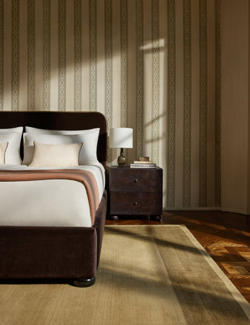 #color::ivy | A velvet upholstered platform bed and nightstand sit infront of a wall featuring the Paradiso striped Wallpaper by Jake Arnold