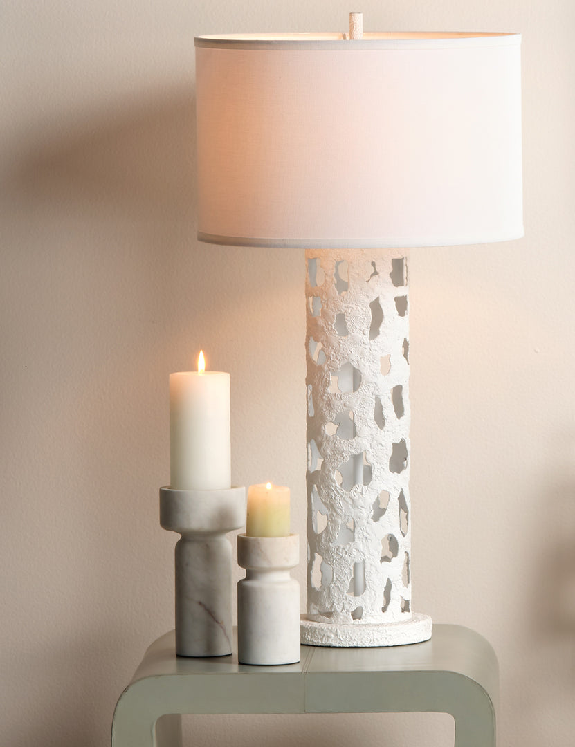 #color::white | Maris sculptural modern pillar candle holder styled next to a table lamp on a side table.