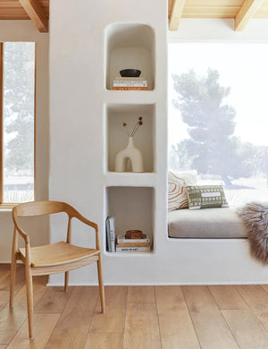 A Natural Ida Dining Arm Chairs sits to the left of recessed wall shelf and a corner nook with a cushioned bench
