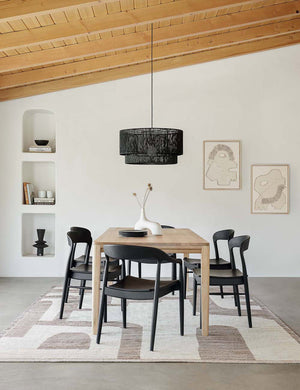 Five Black Ida Dining Arm Chairs sit around a rectangular wooden dining table beneath a black jute chandelier and wooden ceiling