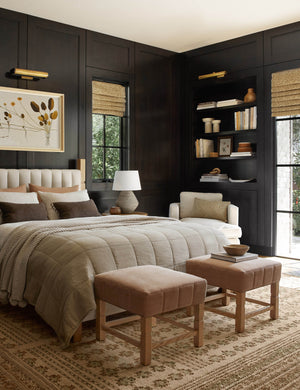  Two Ambleside apricot linen ottomans sit at the edge of a bed with a book and a wooden bowl atop a patterned rug