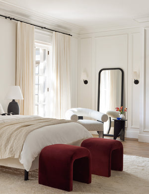 Two Paprika Velvet Tate Stools sit at the end of a bed with an arched headboard atop a plush rug