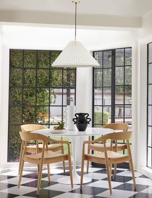 Four Natural Ida Dining Arm Chairs sit around a circular white dining table in a room with a black and white checkerboard floor