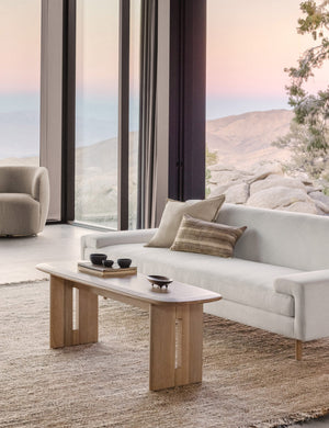 The Henrik light wood bench sits atop a jute rug in front of a white linen sofa in a room with floor to ceiling windows